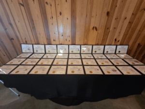 May show: A table covered with a black cloth displays numerous framed certificates against a wooden wall.